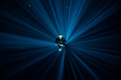 A freediver is shown underwater in the centre of a circular light beam
