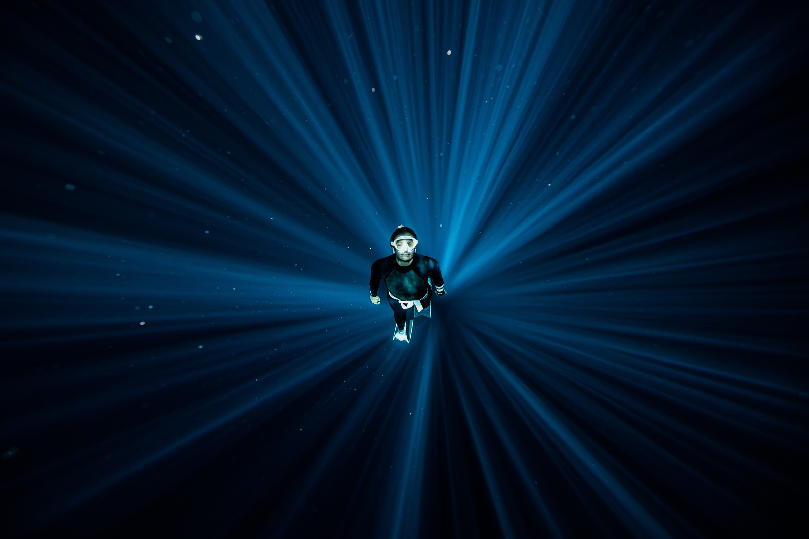 A freediver is shown underwater in the centre of a circular light beam