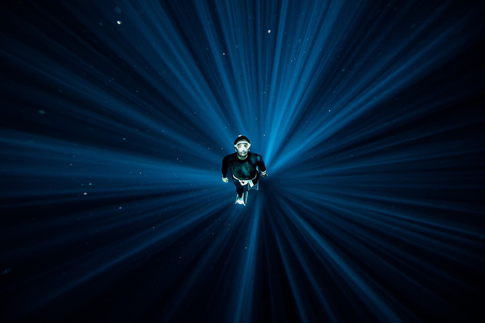 A freediver is shown underwater in the centre of a circular light beam