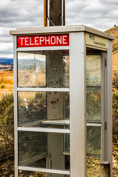 A phone booth and telephone pole in a rural setting.