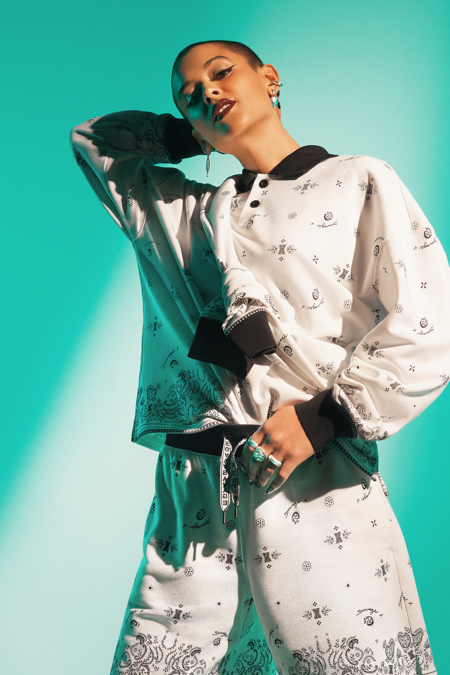 Canadian actress and singer, Jordan Alexander, wearing a white long sleeve, collared shirt and matching long shorts, posing against a vibrant teal backdrop