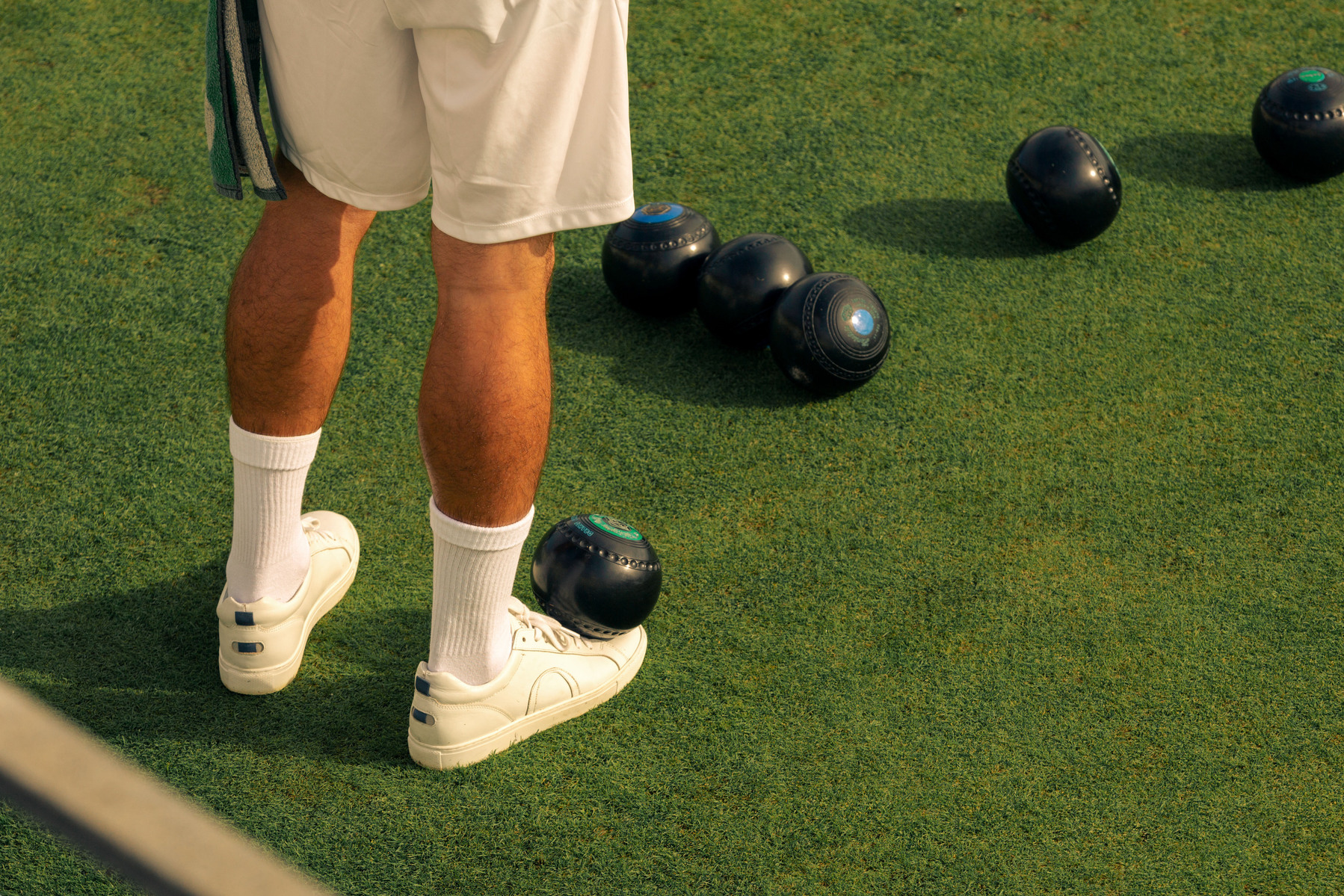 Newquay West End Bowls Club playing at their location above the Newquay harbour, in Cornwall, Western England. A young man balances a bowls ball on his right foot.