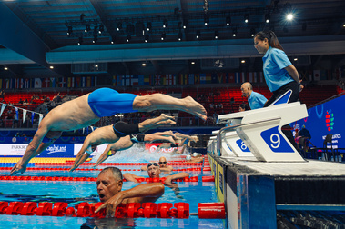 Masters swimmers launch into a race from the starting blocks while exhausted competitors from the previous heat hold the lane ropes and catch their breath in the pool. World Aquatics Singapore Masters Championships 2025.