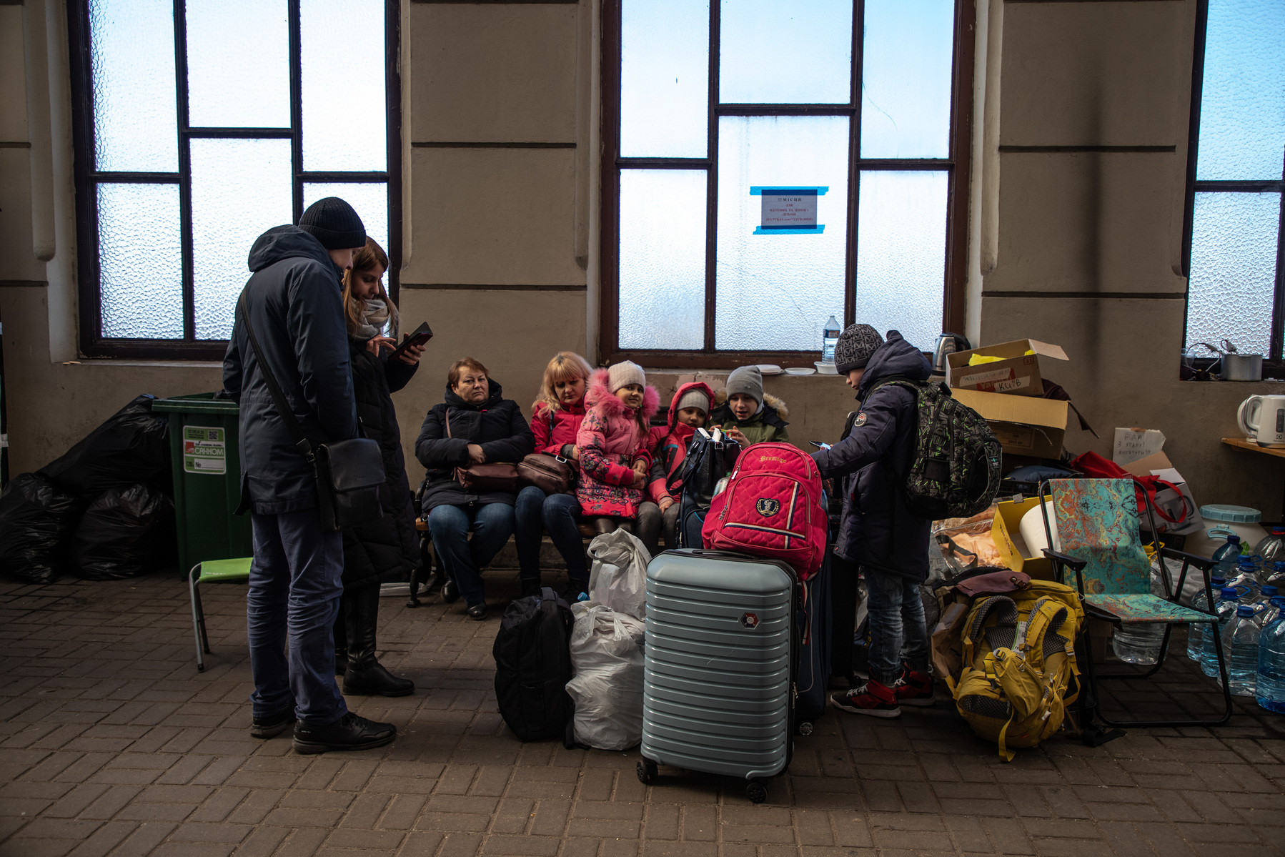 Tania mira su teléfono junto a su esposo Vitalik y sus hijos en la estación de Lviv, Ucrania.  Fotografía de Claudia Paparelli