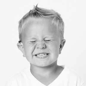 toddler boy with cochlear smiling so big that his eyes are closed  in black and white