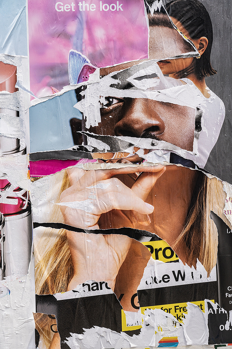 A layered series of torn advertising posters on an urban construction wall create a sculptural effect, a totem of mixed races and genders and scales. The center is a Black male and a White woman's hand. One eye, one nose, two heads. "Get the Look"
