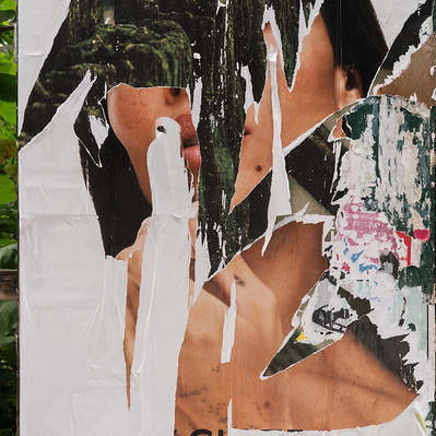 The head and hand of a female POC is obliterated by rips in a poster revealing a dark green exterior scene. Only a partial mouth, one nostril, an ear, and hair appear. Lots of white surrounds the portrait as does actual nature, with green leafy weeds.