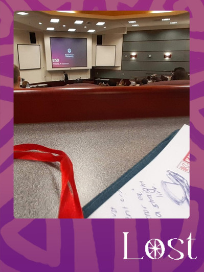 Gallery Image: Text reads: LOST. On a purple border around an image of a university classroom with a brown desk and projection screen in the distance. Along bottom is a red ribbon and the edge of a notebook with penned notes and doodles.