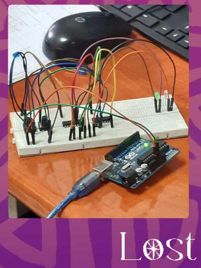 Gallery Image: Text reads: LOST. On a purple border around an image of a wired circuit board that is connected to a green computer chip with a thick blue cord coming out of it. In the top corner are a black computer mouse and keyboard. 