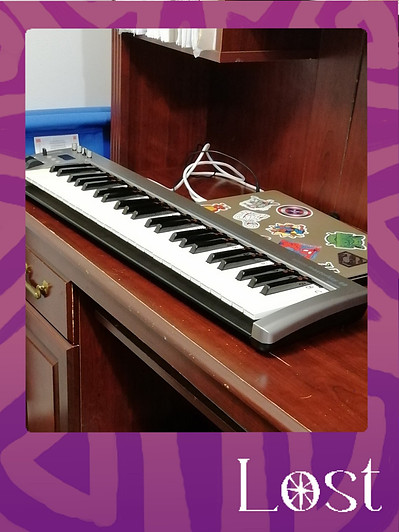 Gallery Image: Text reads: LOST. On a purple border around an image of an electric keyboard and apple laptop computer on a solid wooden desk.