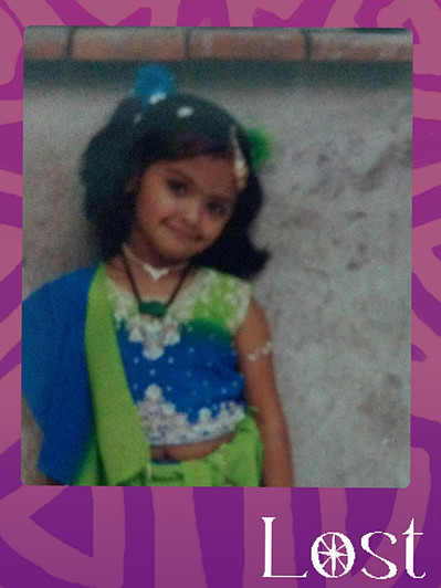 Gallery Image: Text reads: LOST. On a purple border around an image of a young girl wearing a blue and green outfit leaning on a clay wall. The child smiles at the camera with a blue and green pom in her hair.