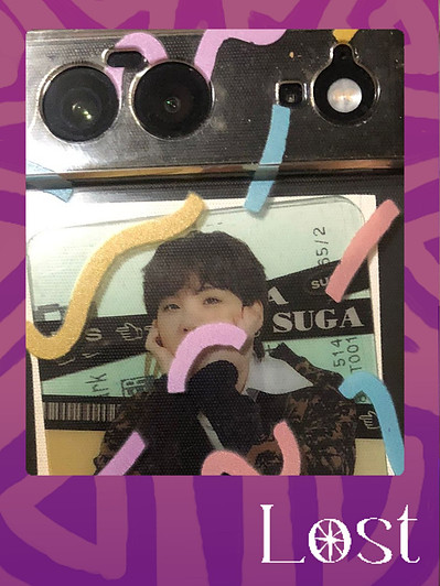 Gallery Image: Text reads: LOST. On a purple border around an image of the backside of a phone. Two cameras & a flash line the top. Through the clear phone case with squiggle lines we see a distorted image of a person with their face on their hand.