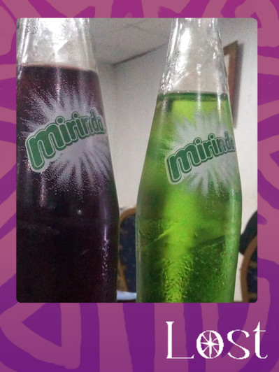 Gallery Image: Text reads: LOST. On a purple border around an image of two glass soda bottles with labels that read: Mirinda. The bottle on the left is filled with a deep purple liquid, the bottle on the right is filled with a bright green liquid.