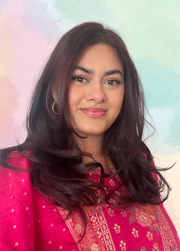 Artist Headshot: Rebecca Fernandes smiles at the camera- her brown hair frames her face, her gold hoop earrings peek out from her hair. She wears a pink shirt with gold and pink embroidery. The backdrop is a water-coloured green, blue, and pink gradient.
