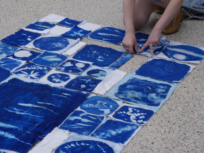 Gallery Image: All previous prints and more are laid out in a grid on a white dotted floor. The blue of the prints is a vibrant contrast to the rest of the image. Two hands are touching the prints at one end of the grid.