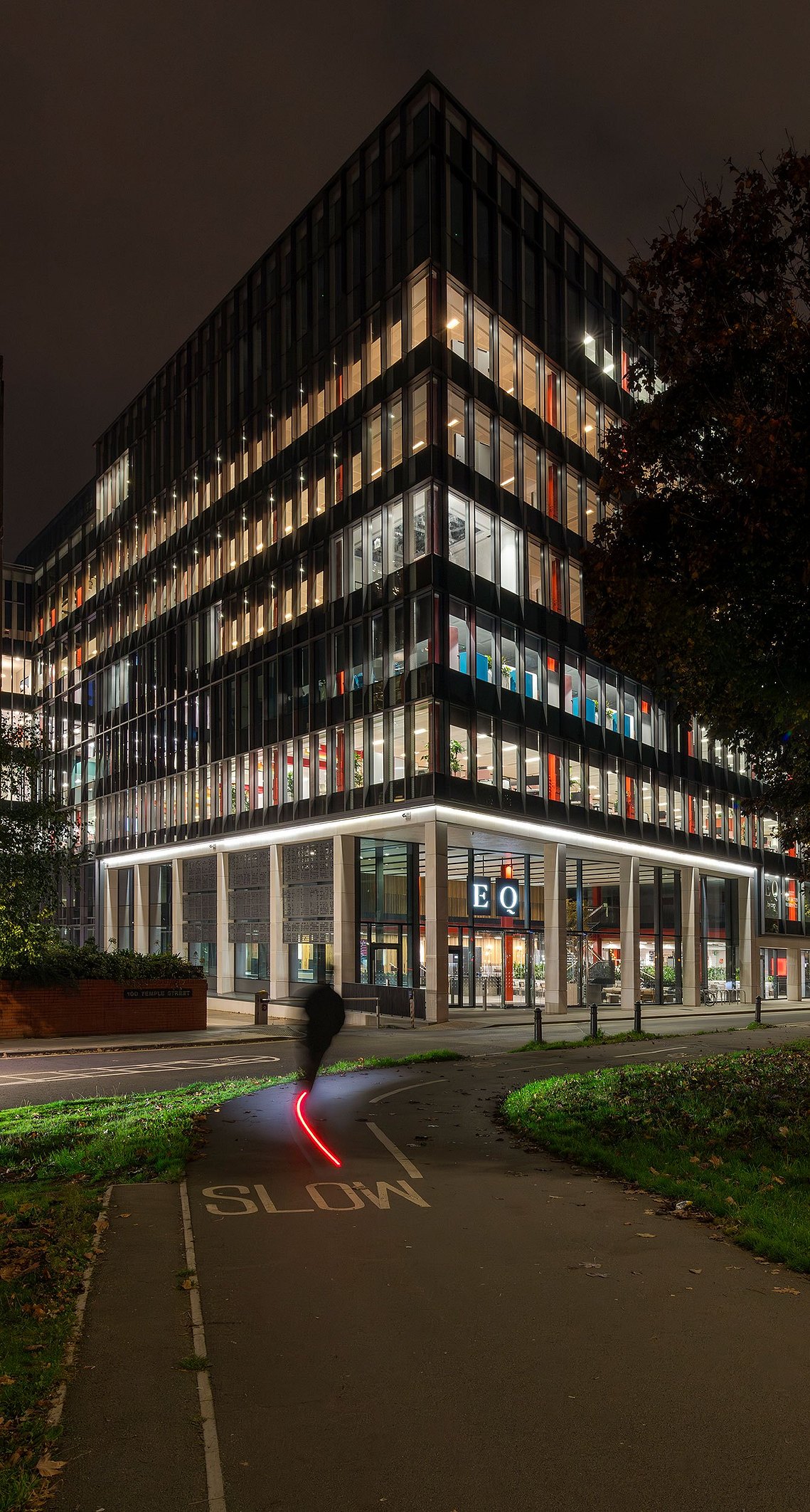 night portrait of modern building illuminated, person rides a scooter in foreground