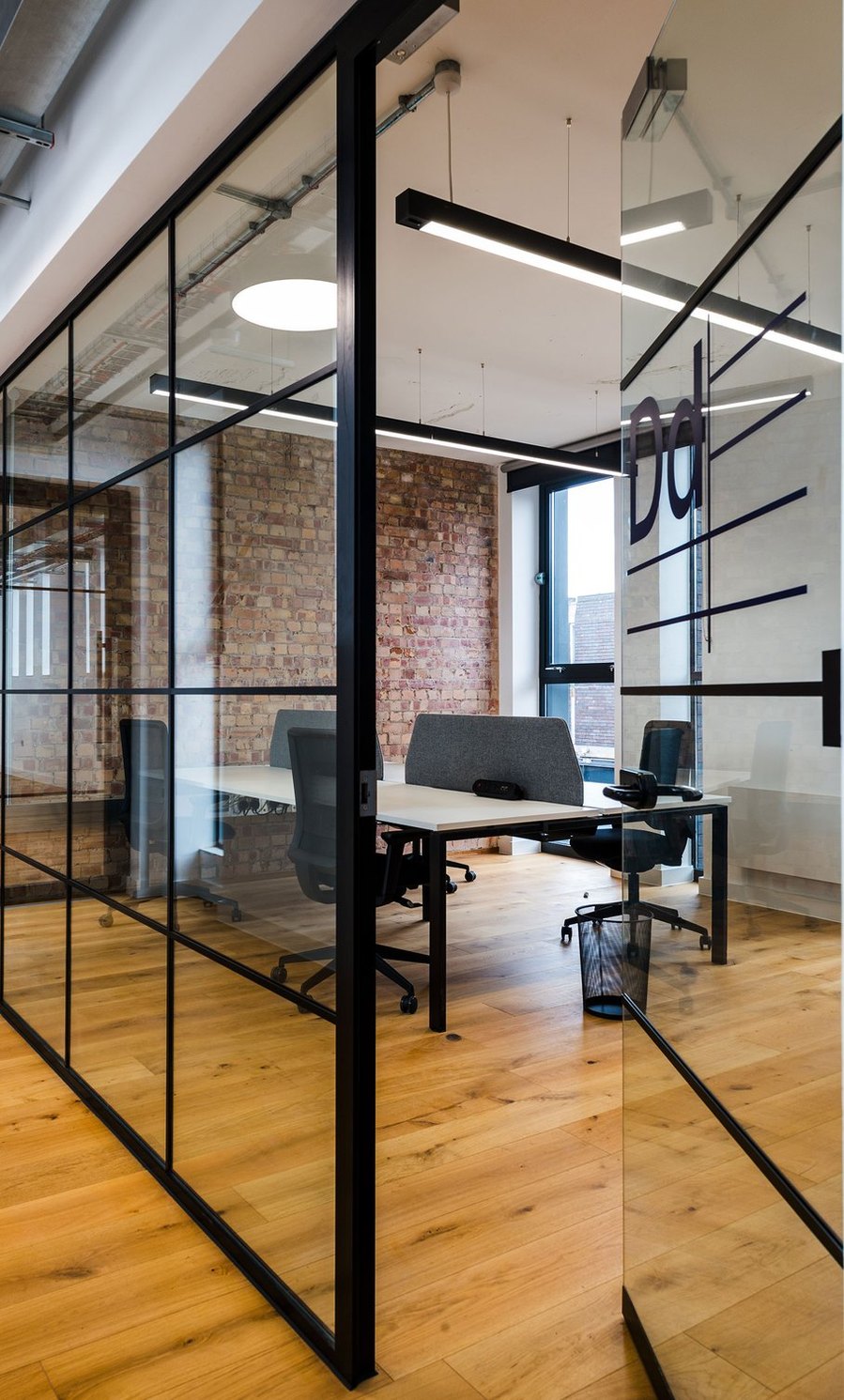 Modern office with glass walls, exposed brick, and wooden floors.