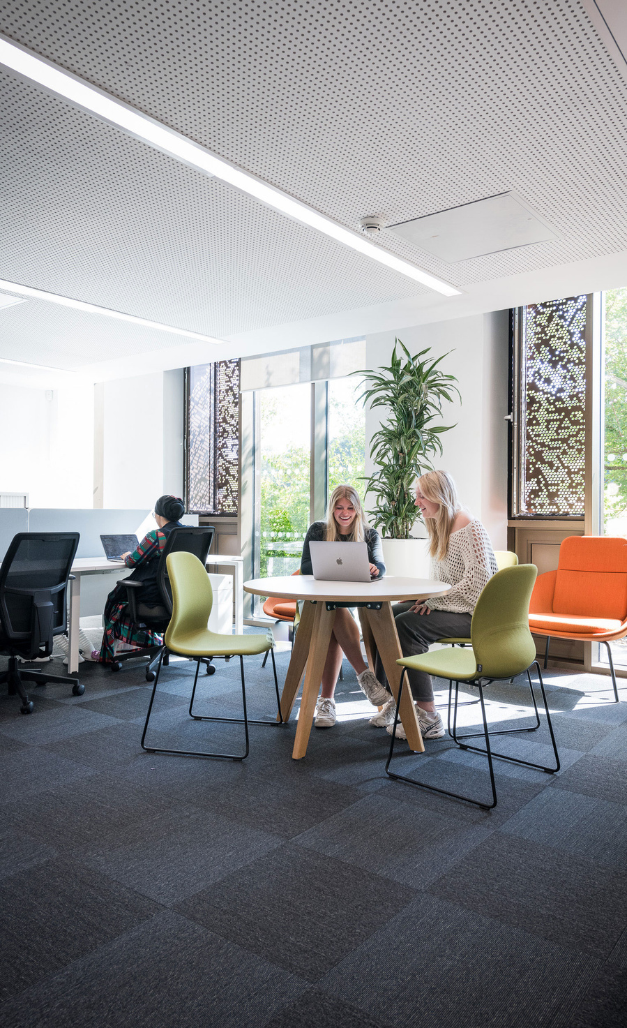 People working in a bright modern office with laptops on desks, surrounded by colorful chairs.