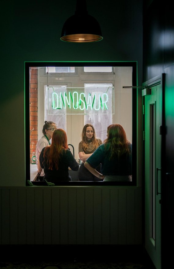 commercial lifestyle photography showing staff in a workplace, candid photograph shot through window, team members stood in kitchen area, neon sign in window 