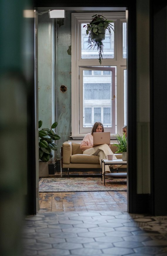 commercial lifestyle photography showing staff in a workplace, candid photograph shot through doorway showing team members sat on a sofa discussing work on a laptop