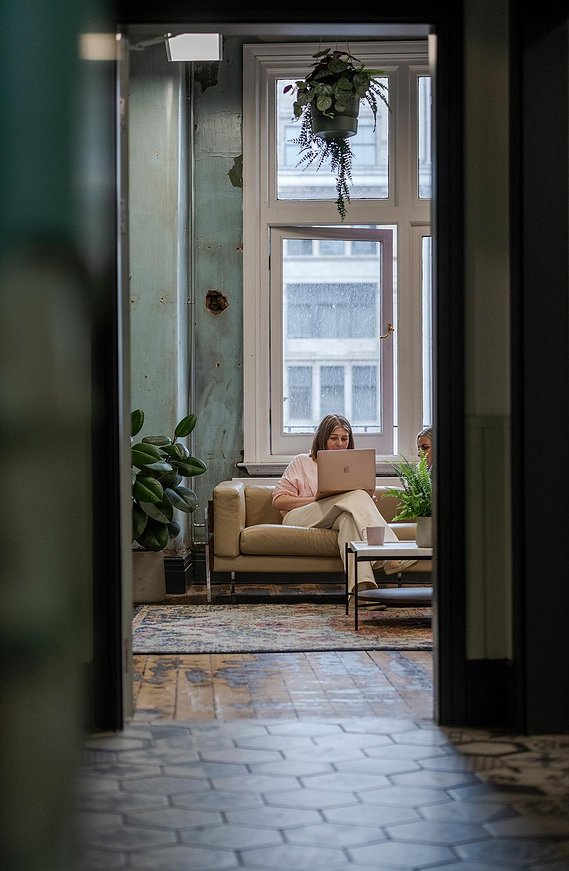 commercial lifestyle photography showing staff in a workplace, candid photograph shot through doorway showing team members sat on a sofa discussing work on a laptop