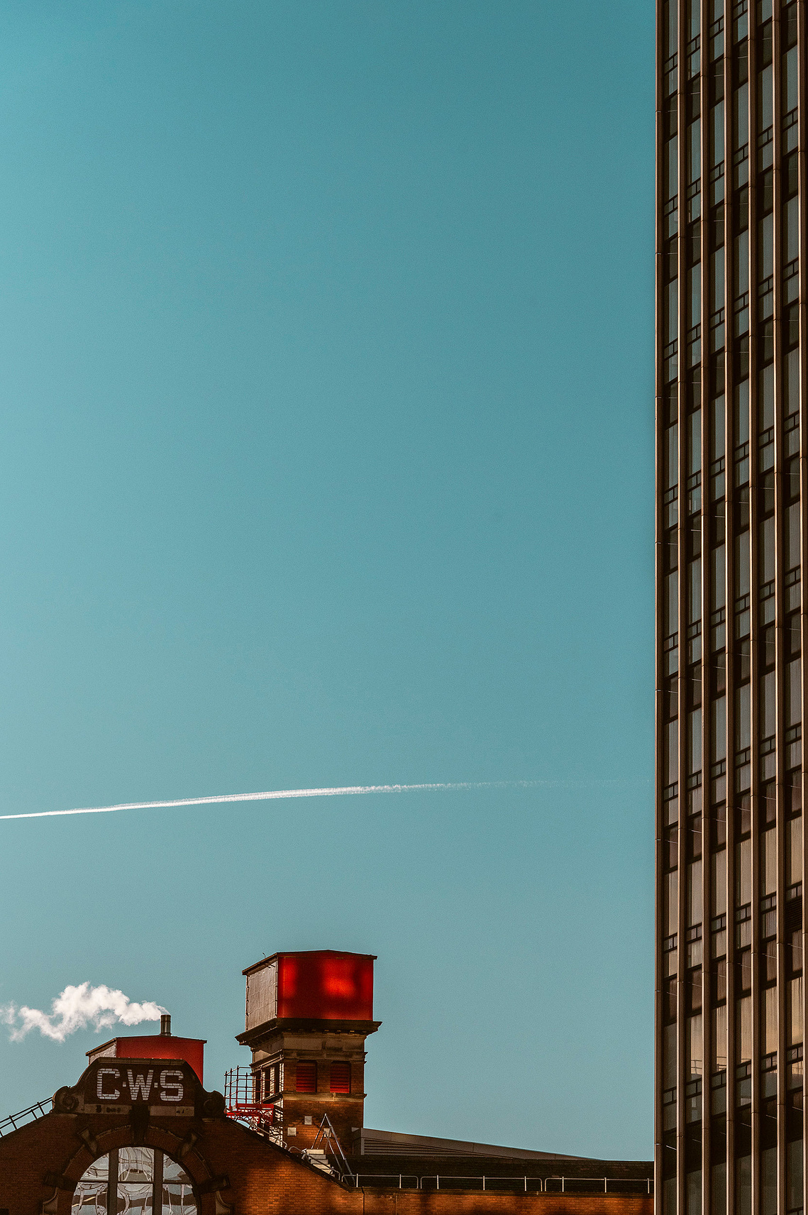 Cropped in Manchester City skyline. Edge of high rise building and rooftop of old factory. Blue sky.
