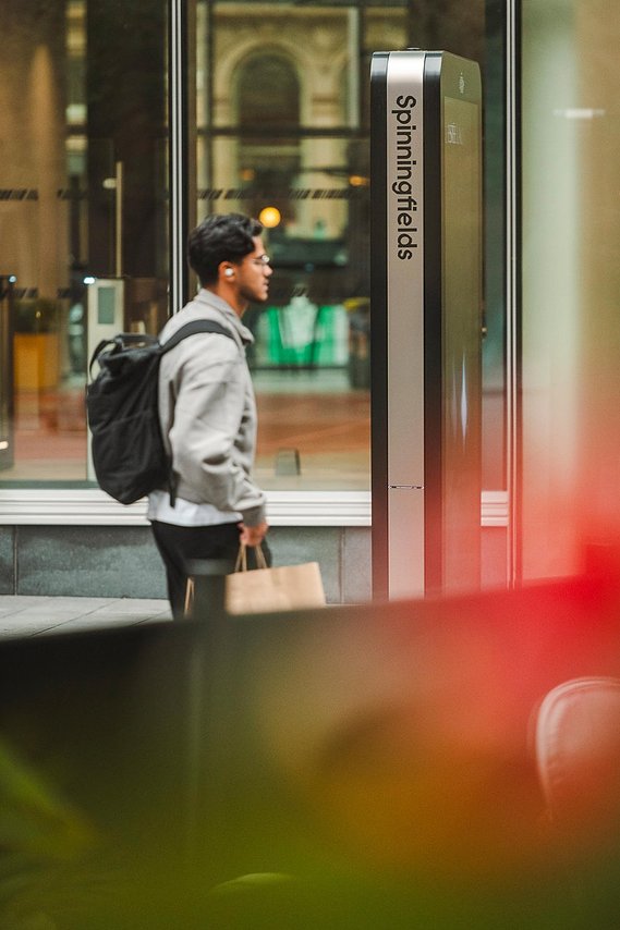 URBAN LIFESTYLE AND LOCAL AREA PHOTOGRAPHY OF SPINNINGFIELDS, MANCHESTER, lifestyle photography showing a shopper with bag walking past signage