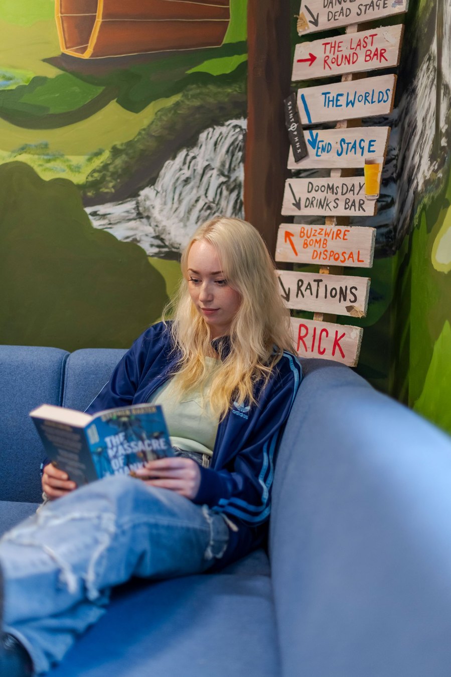 student lifestyle photography, student sits in room with colourful wall murals reading a book