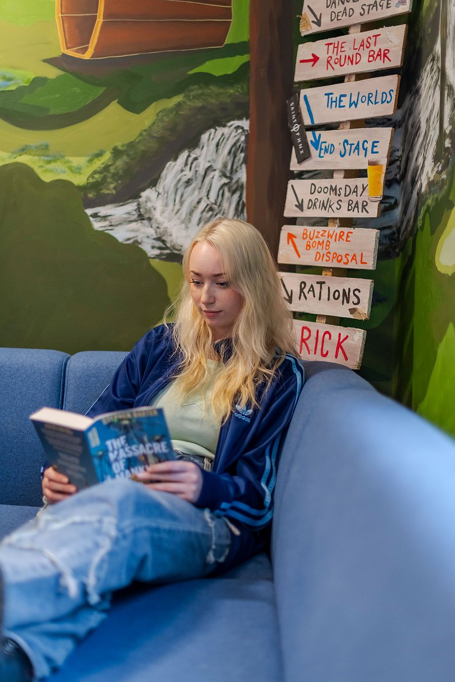 student lifestyle photography, student sits in room with colourful wall murals reading a book