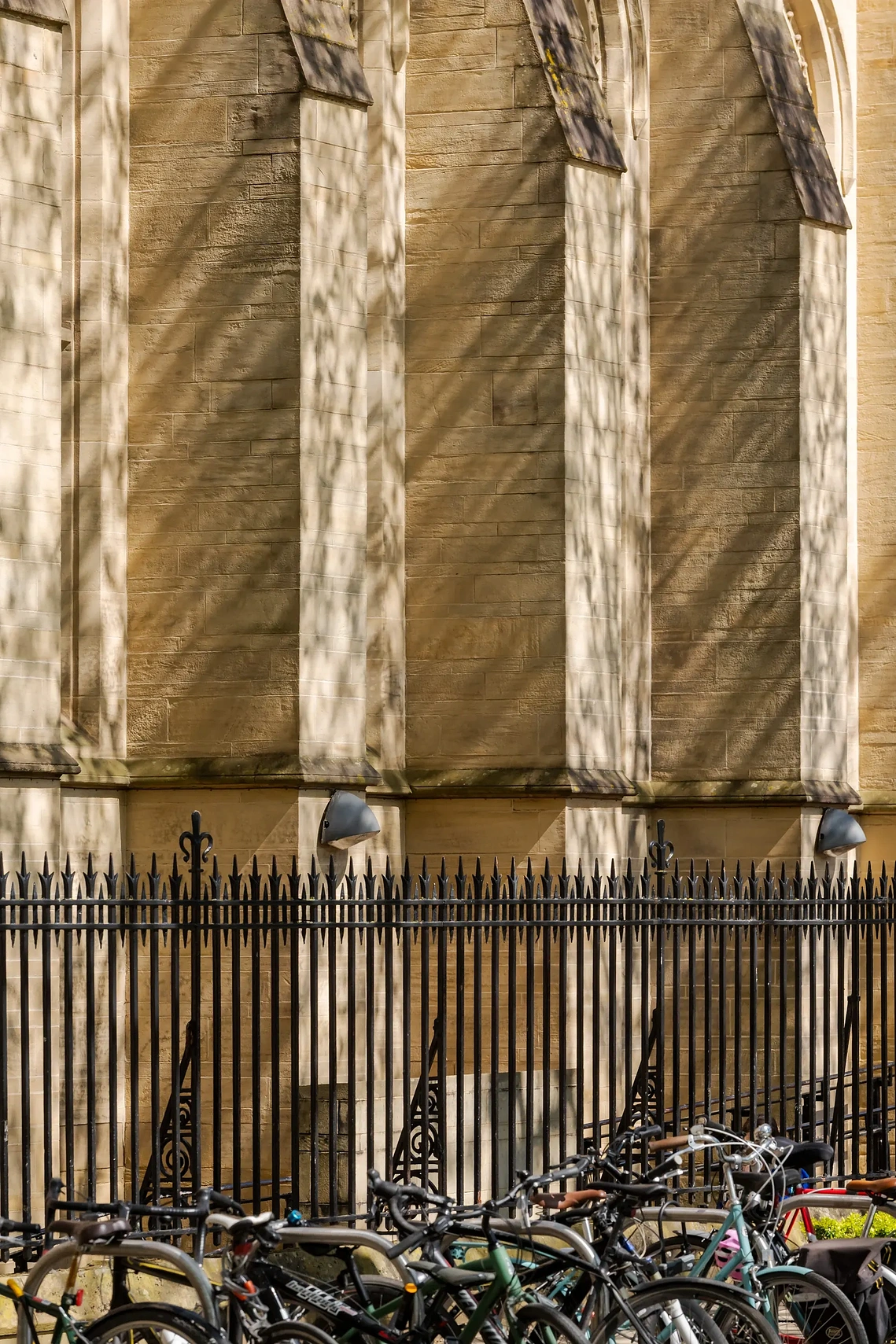 Deep shadows and strong sunlight casting geometric patterns across a building exterior with bicycles