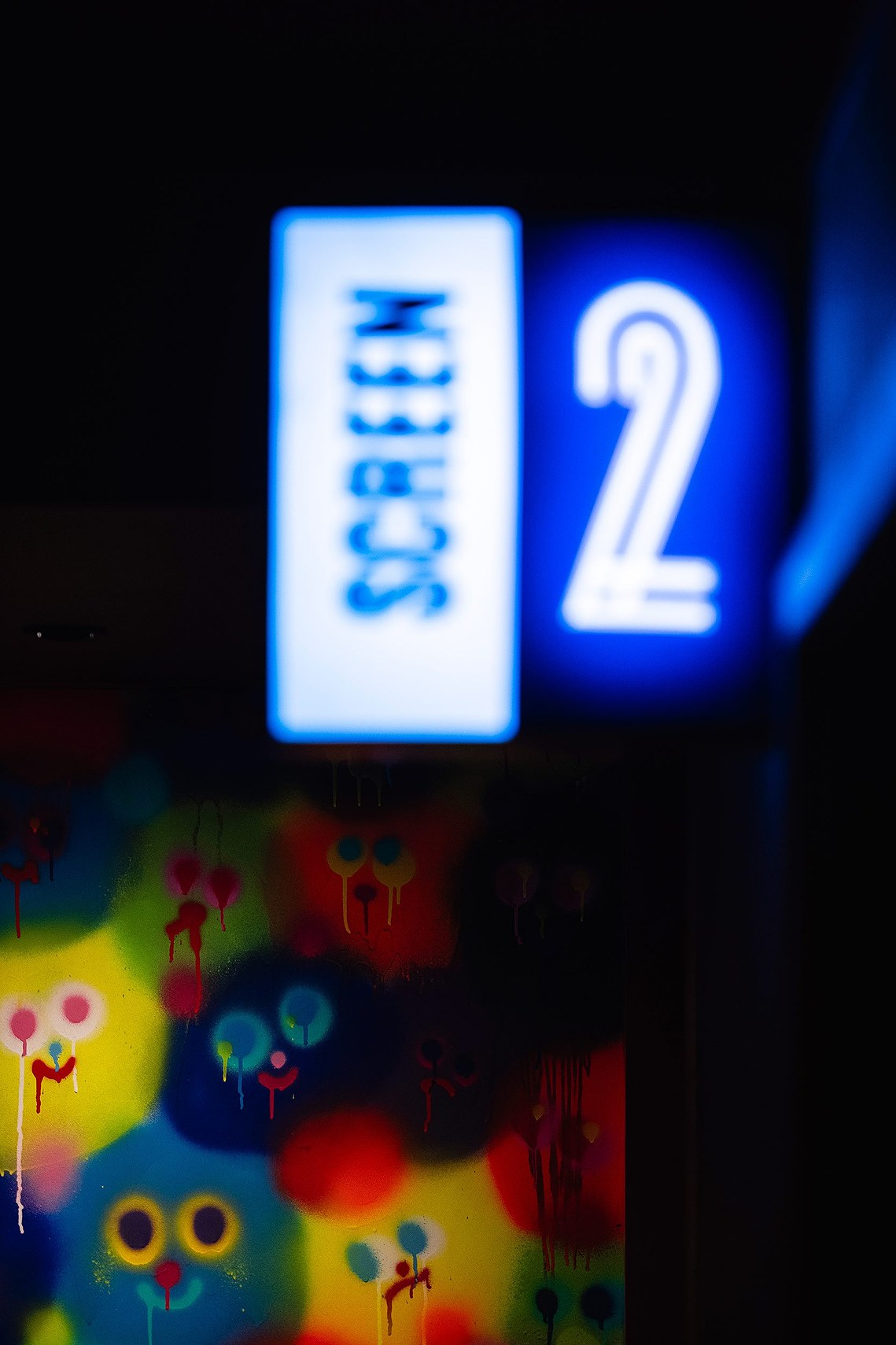 cropped shot of cinema corridor with glowing sign for screen entrance and colourful faces on a mural in background