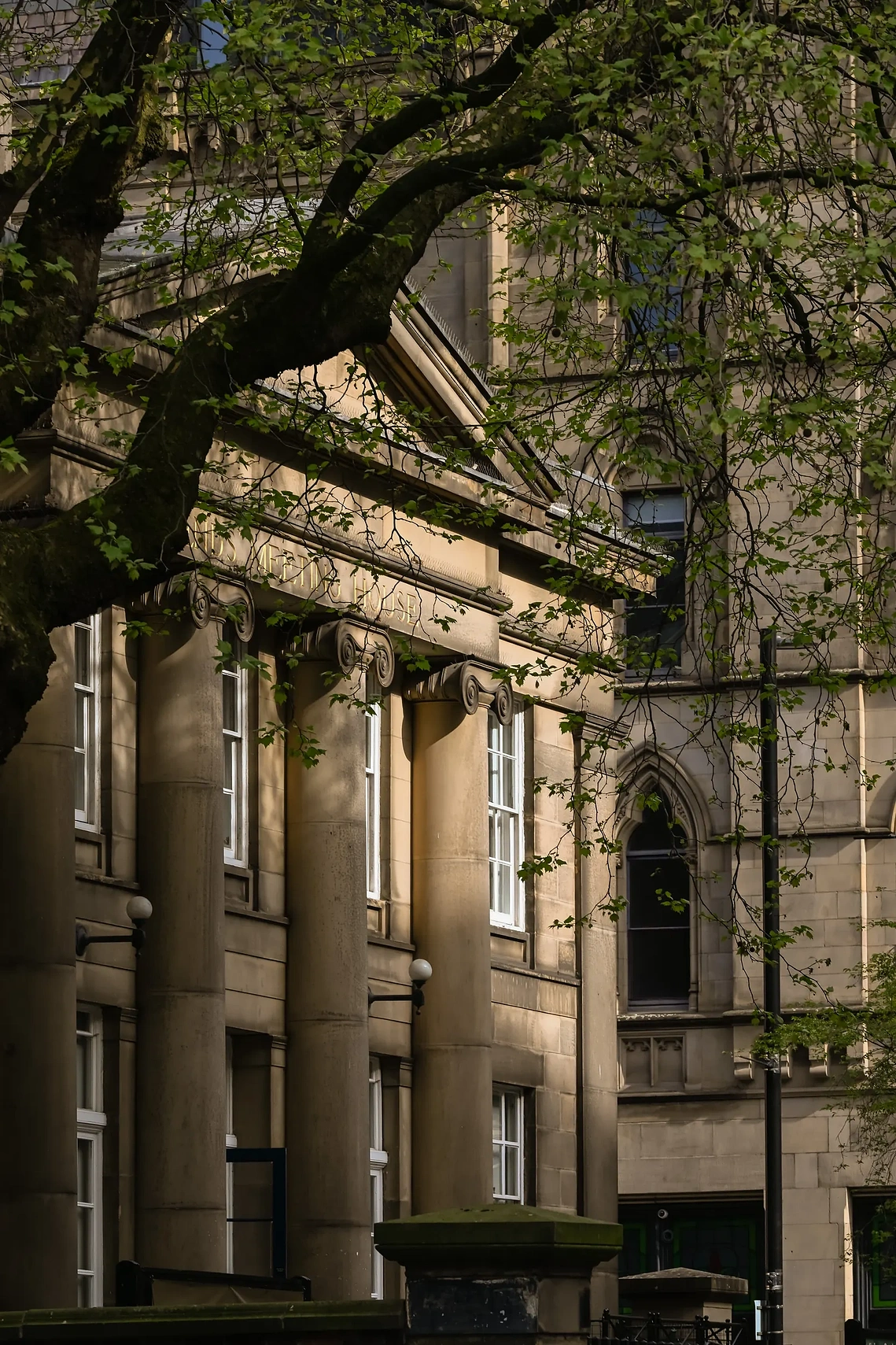 Heritage architecture photograph captured around the campuses of the Manchester universities. Trees and sunlight create shadows
