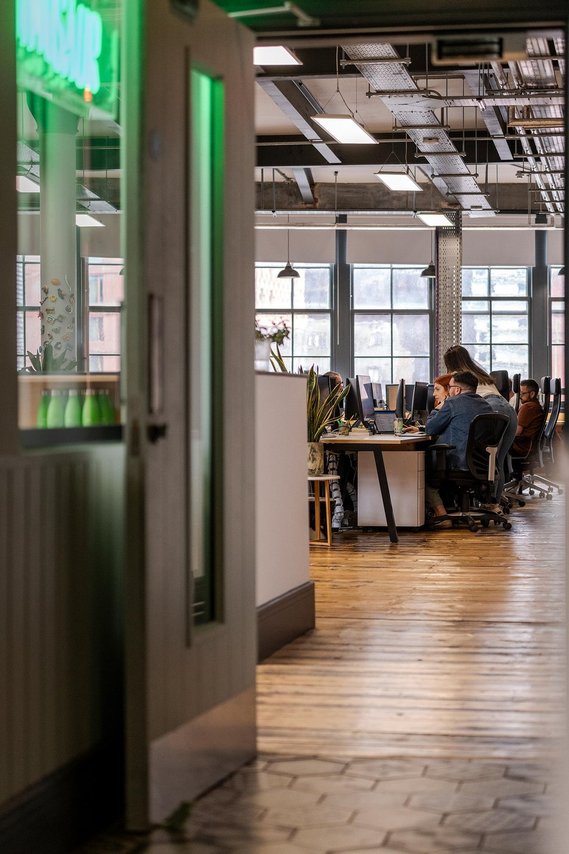 commercial lifestyle photography showing staff in a workplace, candid photograph shot through doorway showing team members sat at desk discussing work