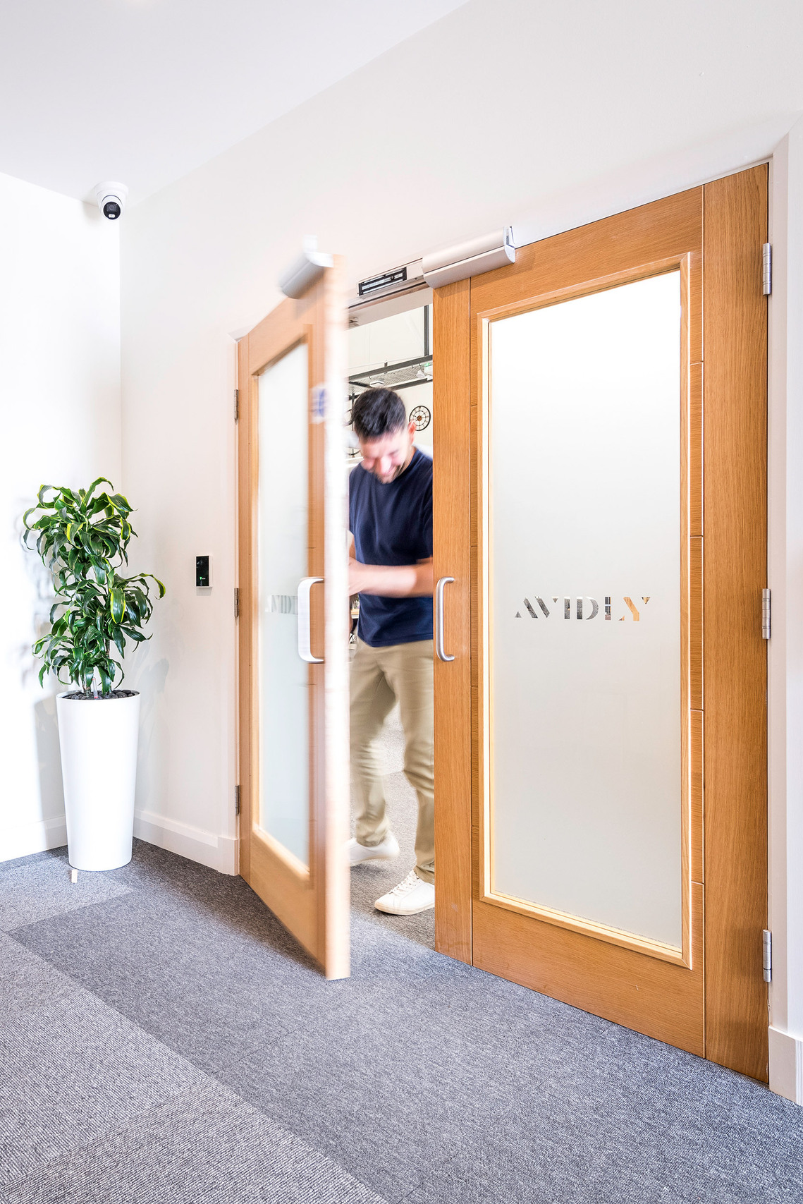 Man walking out of branded glass office door into reception area with plant