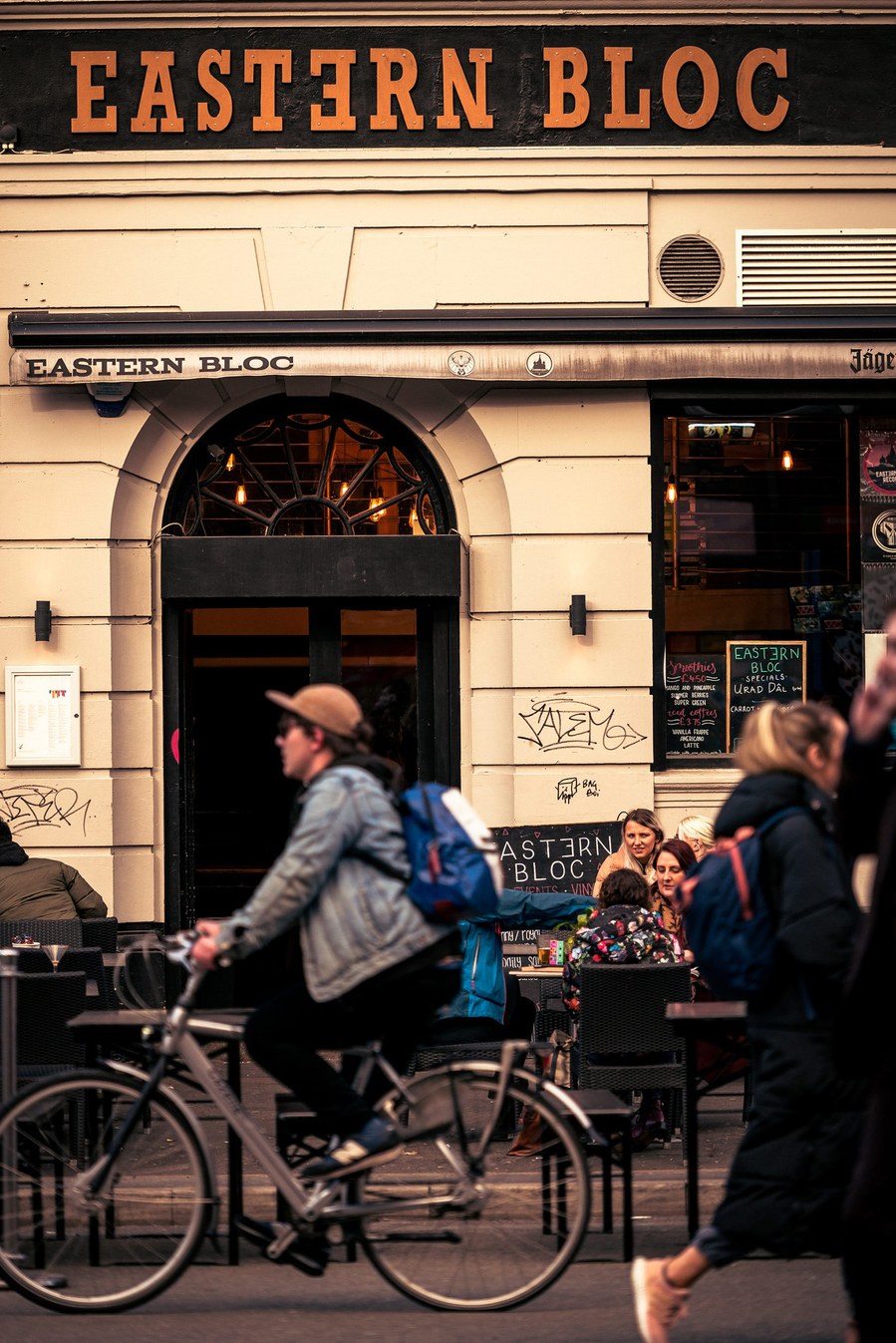 placemaking photography. manchester. norther quarter. architecture. man cycling past bar and record shop 