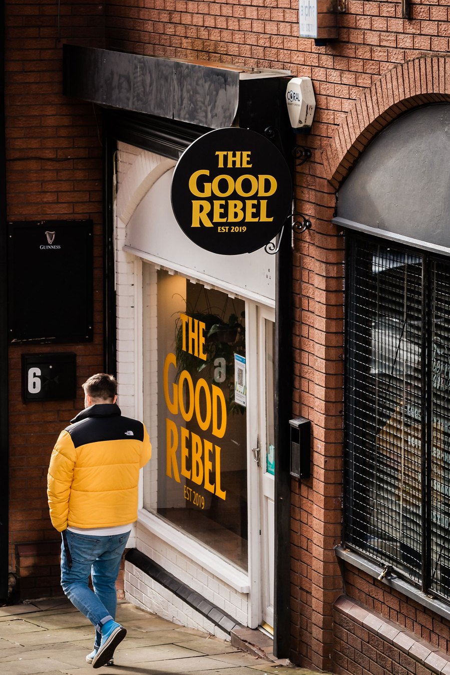 stockport lifestyle and placemaking photography, local street architecture, man in coat walking past bar, yellow