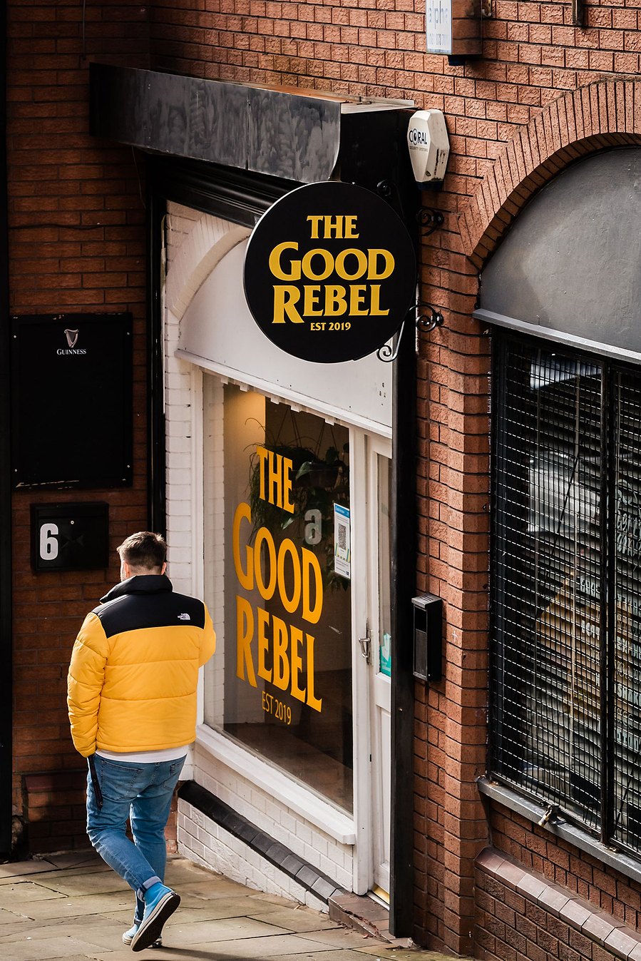 stockport lifestyle and placemaking photography, local street architecture, man in coat walking past bar, yellow