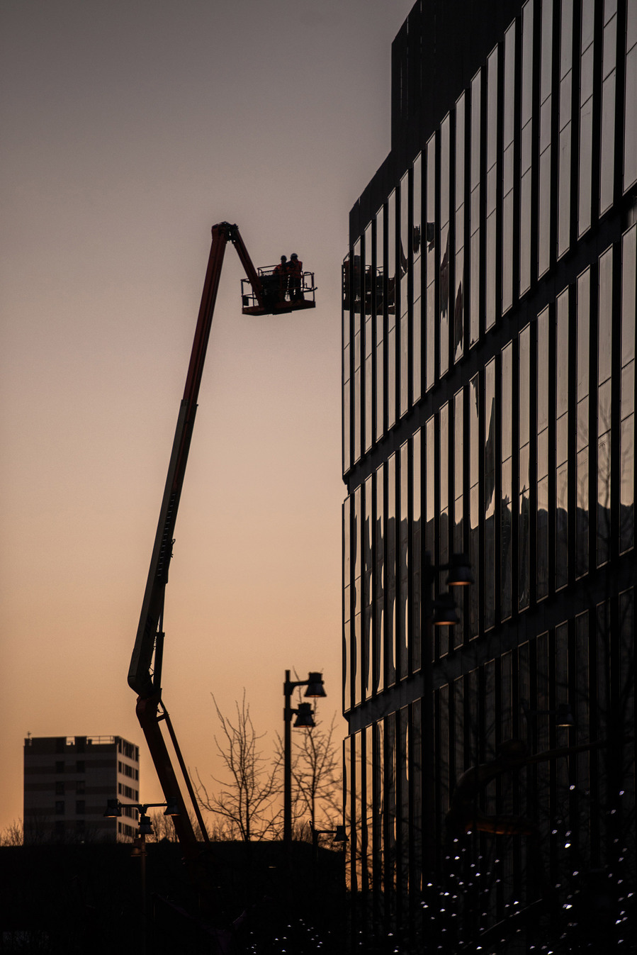 cropped image of modern city buildings against evening sky with cherrypicker and workers