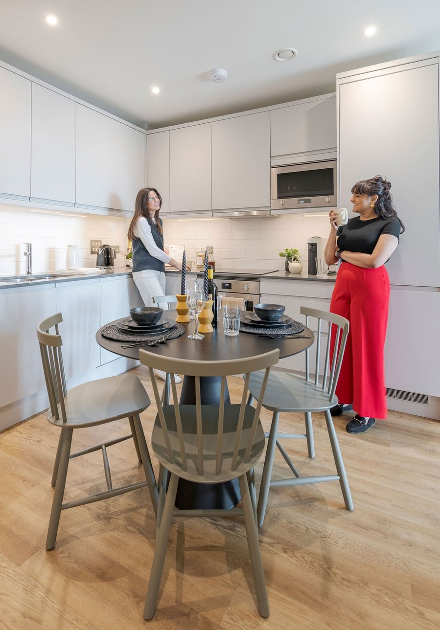 Modern kitchen interior with two people, one holding a mug, and a dining table set for two.