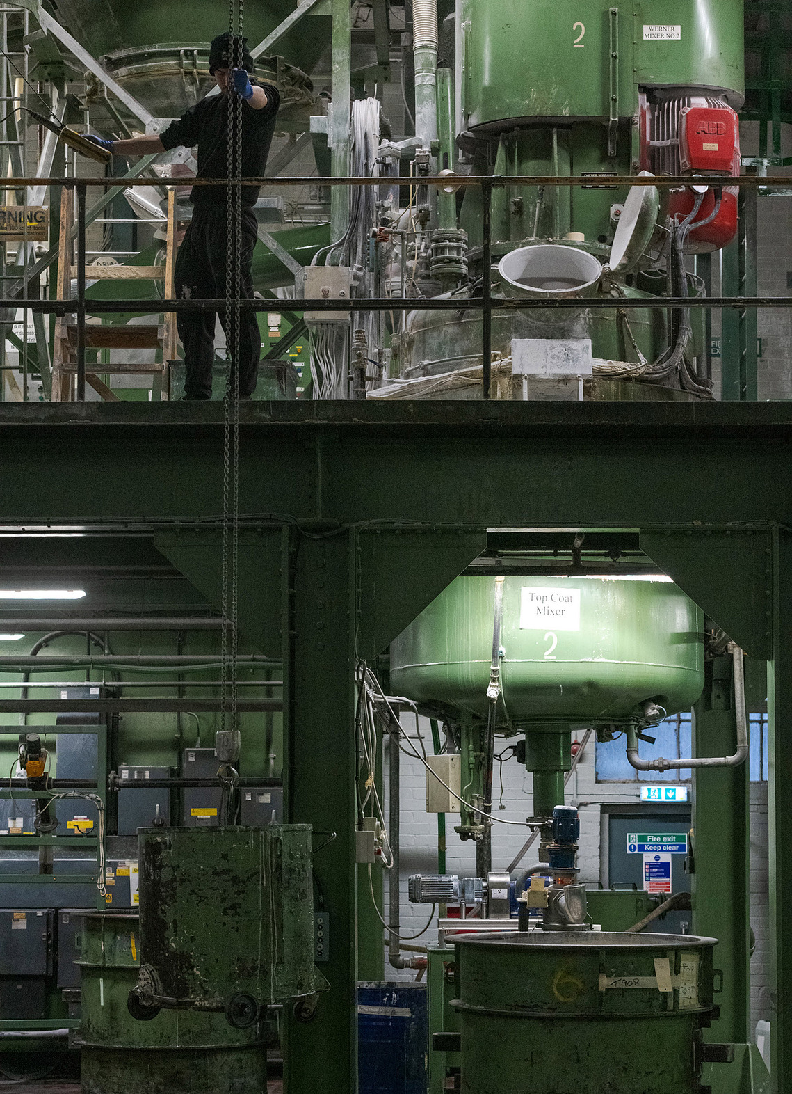 Documentary manufacturing photography capturing a factory worker operating machinery, pipes and paint.
