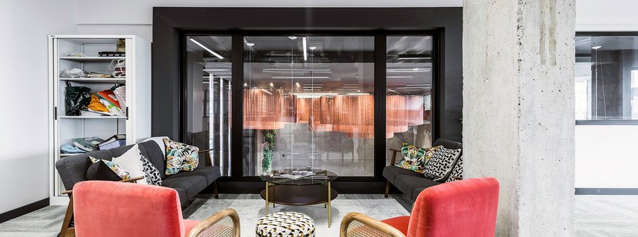 Modern office lounge with red chairs, glass walls, and decorative curtains.