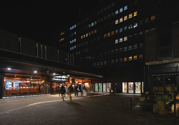 architecture photography, exterior of cinema with lights glowing and people walking through door, tower in background, night time