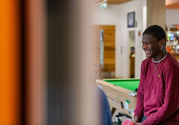 Commercial photography for higher education case study cover showing student laughing and leaning on a pool table