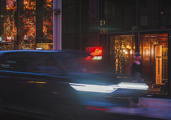 Street photography and lifestyle photography style shot shows a girl waiting outside a restaurant at night as a car drives past
