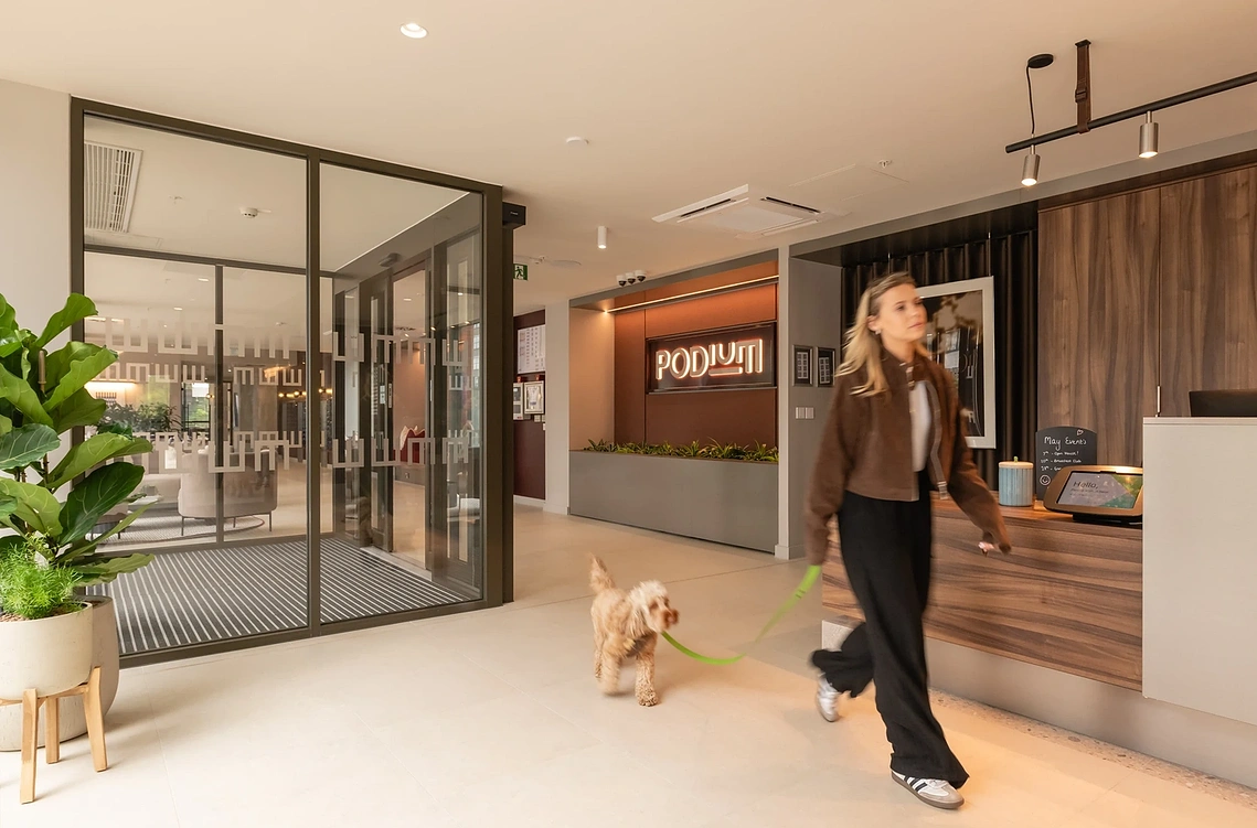 Resident arriving with her dog at Podium's reception, with illuminated signage. Commercial lifestyle photography, Old Trafford.
