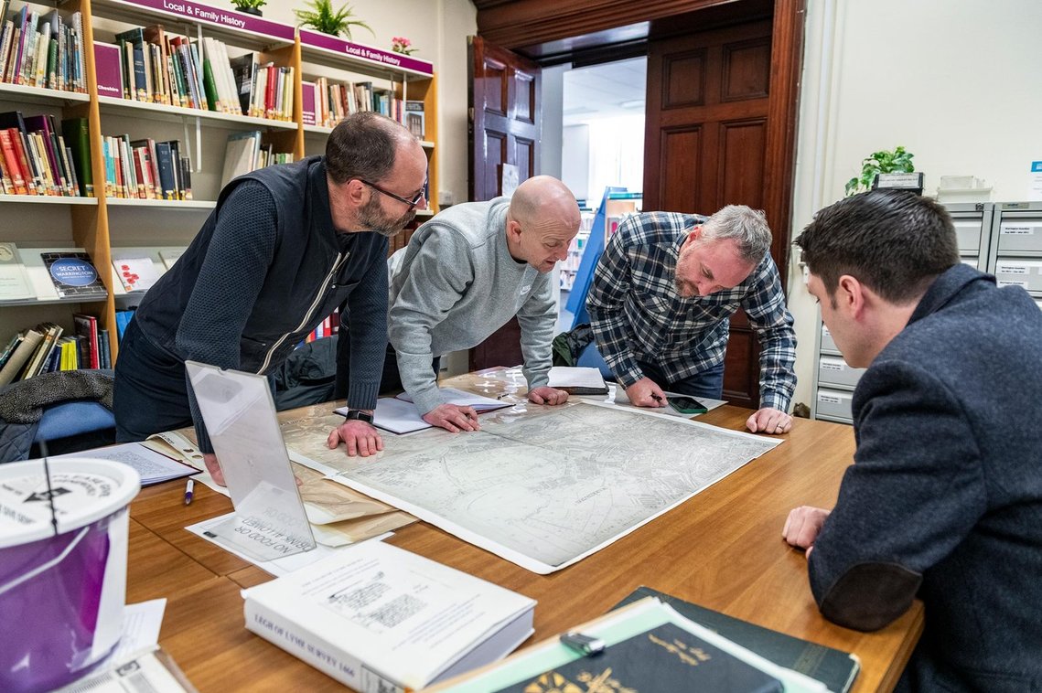 project team meeting with museum archivist and viewing map around table
