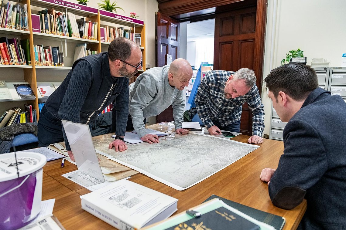 project team meeting with museum archivist and viewing map around table
