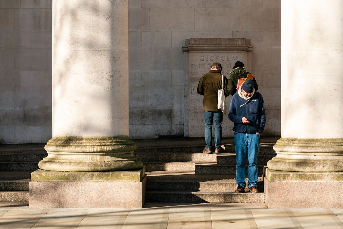 architecture and lifestyle photography showing three men stood either looking away or at their phones, between two grand pillars of a building, 