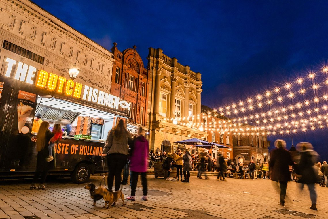 stockport lifestyle photography, evening shot of food market with footfall, fairylights and customers walking dogs