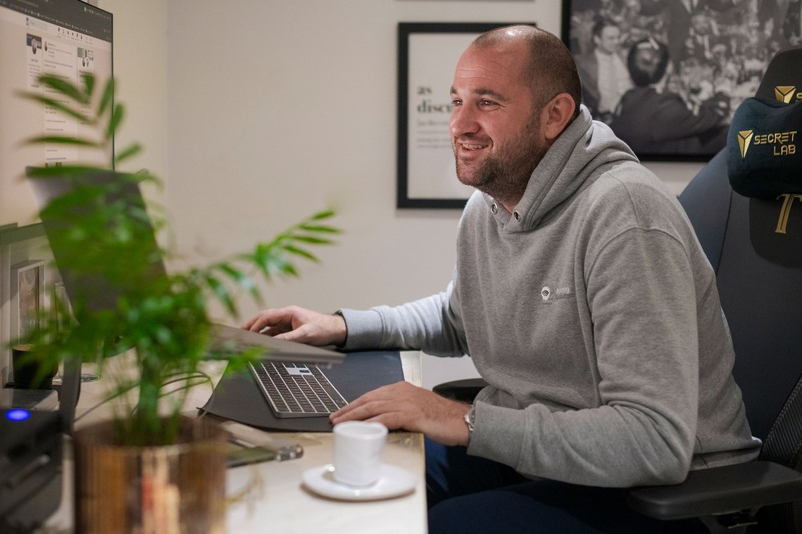 person working from home office, man smiles was he looks at screen. pictures on wall in background 